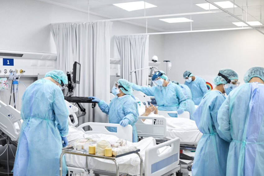 Healthcare coworkers working in ICU. Doctors and nurses wearing protective coveralls. They are at hospital during COVID-19.