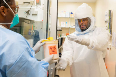 Healthcare worker handing off a specimen to a lab technician in PPE