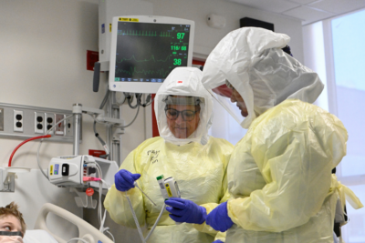 Healthcare workers in PPE checking a patient's vital signs.